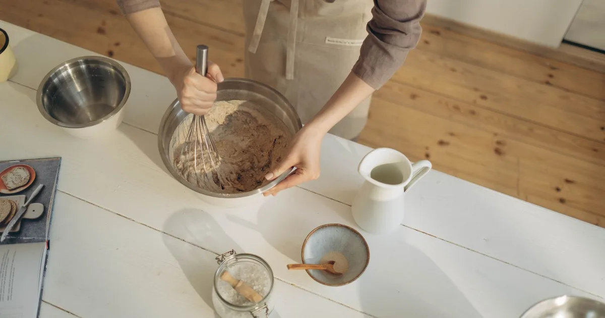 Pâte à crêpes lisse dans un bol en céramique, fouet posé à côté sur un plan de travail en bois